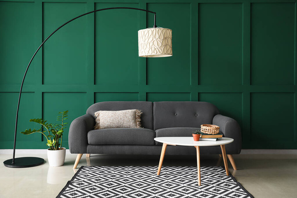 Удобный диван со столом и современной лампой возле зеленой стены - Фото, изображение