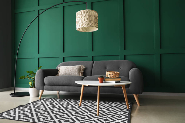 Bequemes Sofa mit Tisch und moderner Lampe in der Nähe der grünen Wand - Foto, Bild