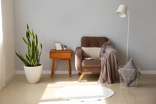 Bequemer Sessel, Zimmerpflanze und Tisch in der Nähe der Lichtwand - Foto, Bild