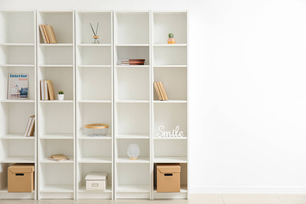 Stylish shelf unit with books and decor elements near white wall - Фото, зображення