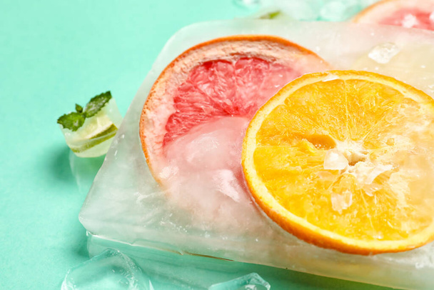 Fresh citrus fruits frozen in ice on turquoise background, closeup - Photo, Image