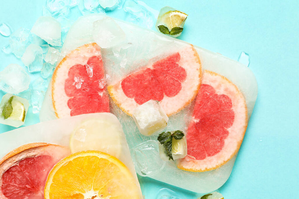 Fresh slices of citrus fruits frozen in ice on turquoise background - Photo, Image