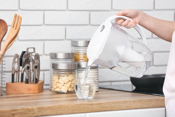 Frau gießt in Küche gereinigtes Wasser aus Filterkrug ins Glas - Foto, Bild