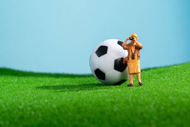 Творческое фото с футбольным мячом на лужайке и туристическим фотографом. Макро-стрельба. Спортивный фон. Миниатюрные люди. - Фото, изображение