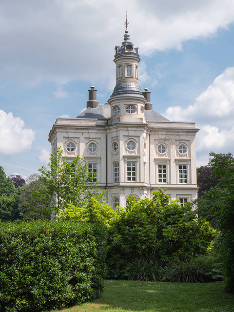 Beveren, Belgium, May 22, 2022, Hof Ter Saksen castle, with blue sky and a field of clouds and in the foreground the garden with tall plants - Photo, Image