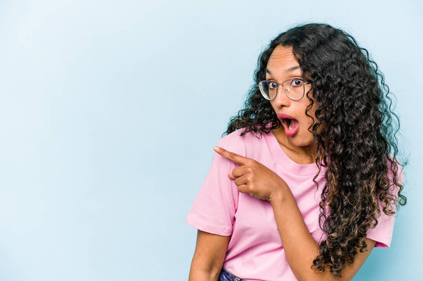 Young hispanic woman isolated on blue background points with thumb finger away, laughing and carefree. - Photo, Image
