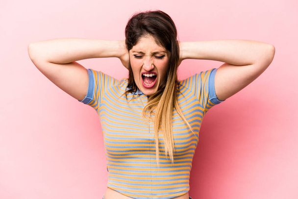 Young caucasian woman isolated on pink background covering ears with hands trying not to hear too loud sound. - Photo, Image