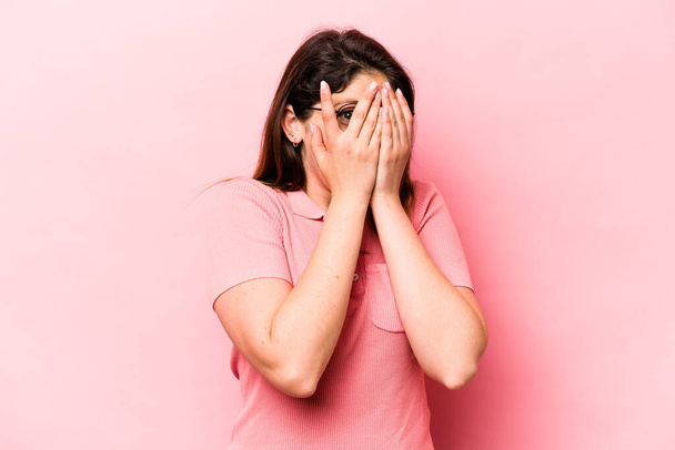 Young caucasian woman isolated on pink background blink through fingers frightened and nervous. - Foto, Imagem