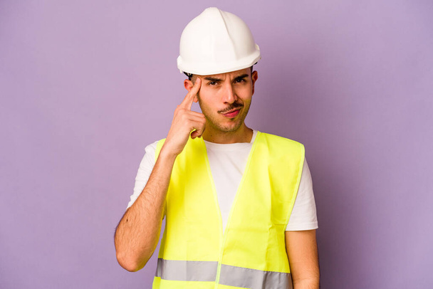 Молодий іспаномовний працівник ізольований на фіолетовому фоні, вказуючи храм пальцем, думаючи, зосереджений на завданні
. - Фото, зображення