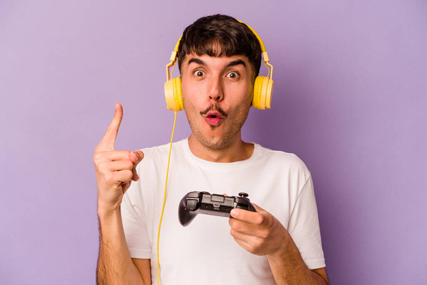 Young hispanic man playing with a video game controller isolated on purple background having some great idea, concept of creativity. - Foto, Bild