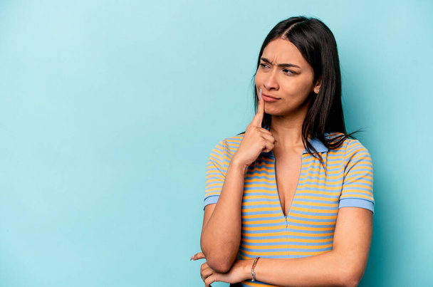 Young hispanic woman isolated on blue background looking sideways with doubtful and skeptical expression. - Photo, Image