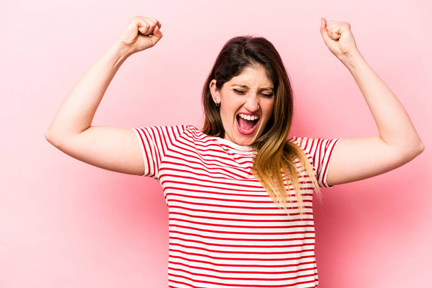 Young caucasian woman isolated on pink background raising fist after a victory, winner concept. - Fotografie, Obrázek