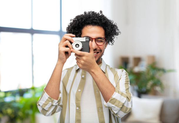 photography, hobby and people and concept - happy smiling man or photographer in glasses with film camera over home room background - Fotó, kép