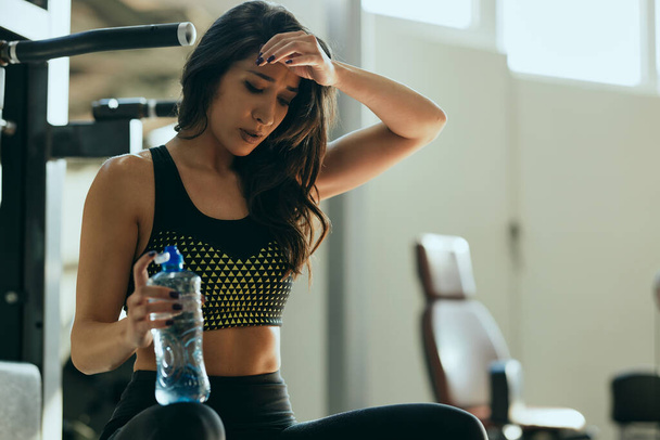 Молода активна жінка відпочиває в спортзалі і п'є воду
. - Фото, зображення