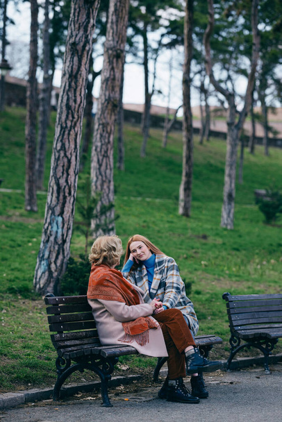 Uma avó está rindo e se divertindo com sua neta adolescente enquanto se senta no banco do parque. - Foto, Imagem