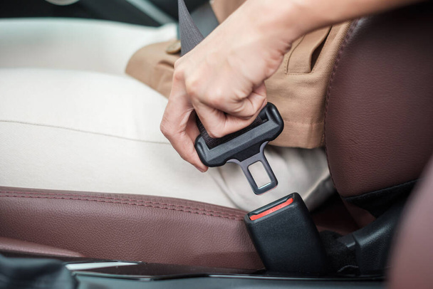 woman driver hand fastening seat belt during sitting inside a car and driving in the road. safety, trip, journey and transport concept - Photo, image