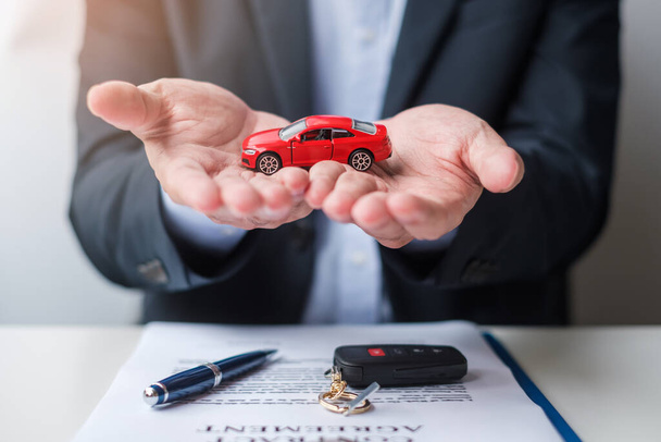 Businessman hand holding red car toy with vehicle keyless, pen and contract document. buy and sale, insurance, rental and contract agreement concepts - Fotó, kép