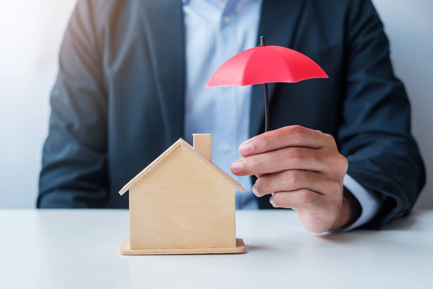 Businessman hand holding red Umbrella cover wooden Home model. real estate, insurance and property concepts - Photo, Image