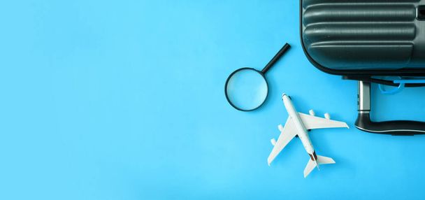 Travel flat lay composition of suitcase with airplane, magnifier on blue background. Prepare trip concept. Banner. - Φωτογραφία, εικόνα