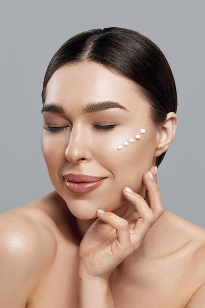 Beautiful smiling woman with healthy smooth facial clean skin applying cosmetic cream and touch own face. Model with  Beauty face. Skin care Moisturizer Facial treatment. Cosmetology. Spa. - 写真・画像