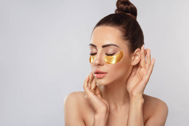 Beauty model girl face with healthy fresh skin. Woman with under eye collagen gold pads.  Skin care concept, anti-aging moisturizing eye mask, golden hydrogel patches, eye skin treatment, cosmetology - Foto, imagen
