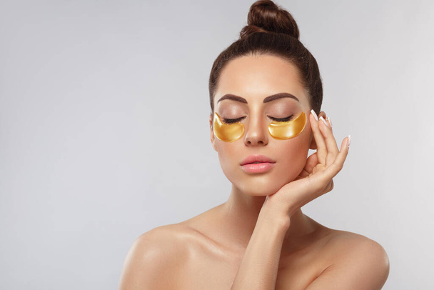 Beauty woman face with under eye collagen gold pads.  Anti-aging moisturizing eye mask, golden hydrogel patches, eye skin treatment, cosmetology - Photo, image