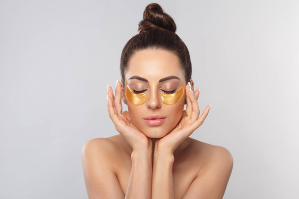 Beautiful woman with healthy perfect skin holds patchs. Beauty face with gold cosmetics collagen hydrogel patch. Lifting anti-wrinkle mask under eyes. Skincare concept - Foto, Imagem