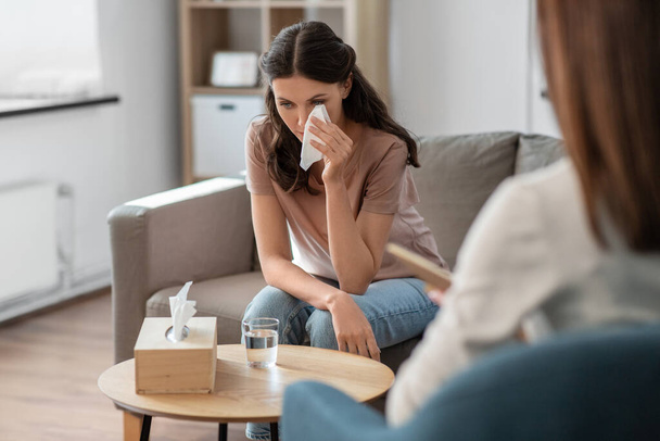 psychology, mental health and people concept - crying woman patient wiping tears with paper tissue and psychologist at psychotherapy session - Foto, Bild