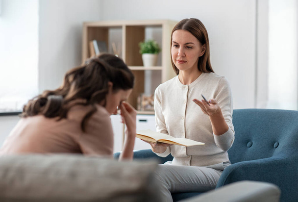 psychology, mental health and people concept - psychologist with notebook talking to stressed woman patient at psychotherapy session - Φωτογραφία, εικόνα