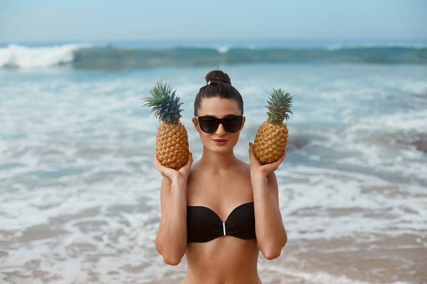 Beautiful Woman with bronze tan in bikini holds pineapples in hands - Photo, image