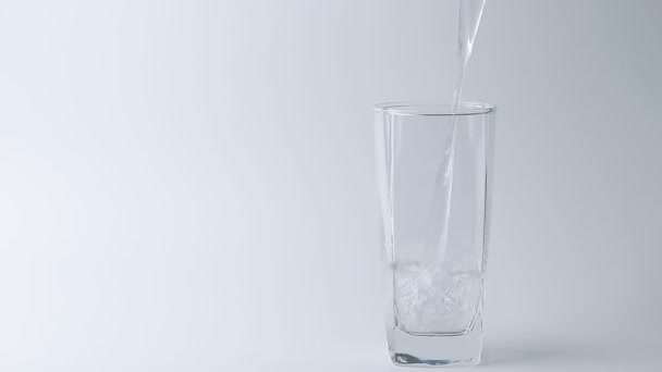 χύνοντας το ποτό γλυκού νερού στο ποτήρι σε γκρι φόντο. Χυνόμενο νερό - Πλάνα, βίντεο