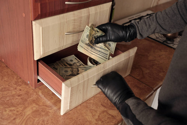 Robber in abito nero e guanti vedere in mensola aperta in cucina. Il ladro preleva le banconote da un ripiano della cucina - Foto, immagini