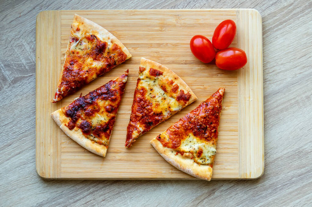 Čtyři plátky pizzy a rajčat na dřevěné desce, porce jídla. - Fotografie, Obrázek