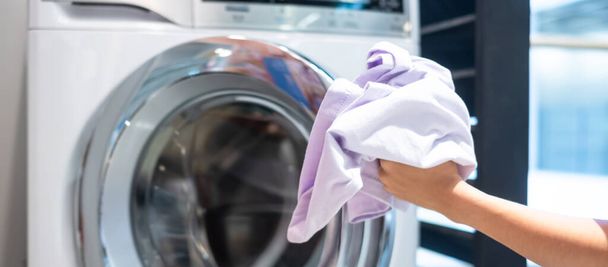 Ama de casa Mujer sosteniendo la ropa dentro de la lavadora en la sala de lavandería
 - Foto, imagen