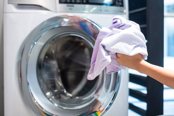 Vrouw vrouw hand houden kleren binnen wasmachine in wasruimte - Foto, afbeelding