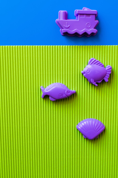 vrchní pohled na fialové mořské živočichy a nádoby hračky na modrém a zeleném pozadí - Fotografie, Obrázek