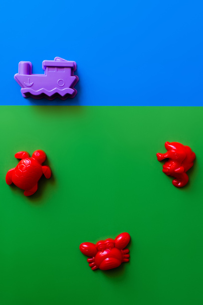 top view of red sea animals and purple ship toys on blue and green background - Photo, Image