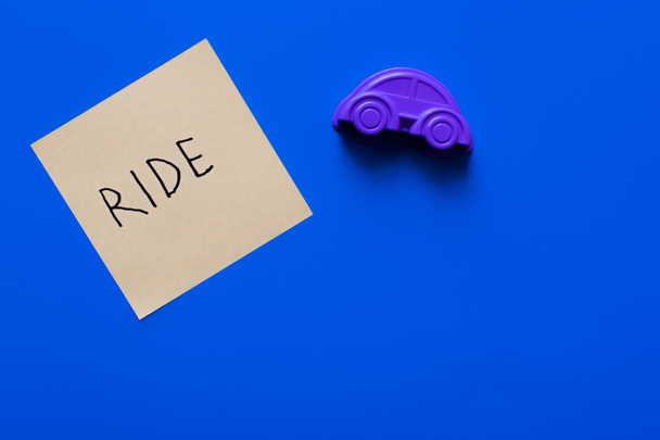 Draufsicht auf Papier mit Aufschrift in der Nähe von lila Spielzeugauto auf blauem Hintergrund - Foto, Bild