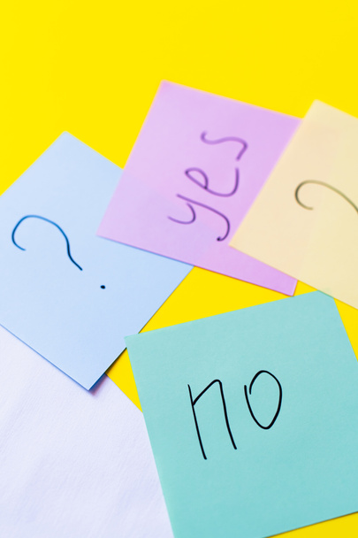 top view of paper notes with question mark near yes and no lettering on yellow background - Foto, imagen