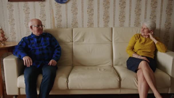 上級関係問題の概念。2人の高齢者ヨーロッパの退職年金受給者のカップルは、居心地の良い古いスタイルのアパートで遠く離れて革ベージュのソファに座っています。高品質4k映像 - 映像、動画