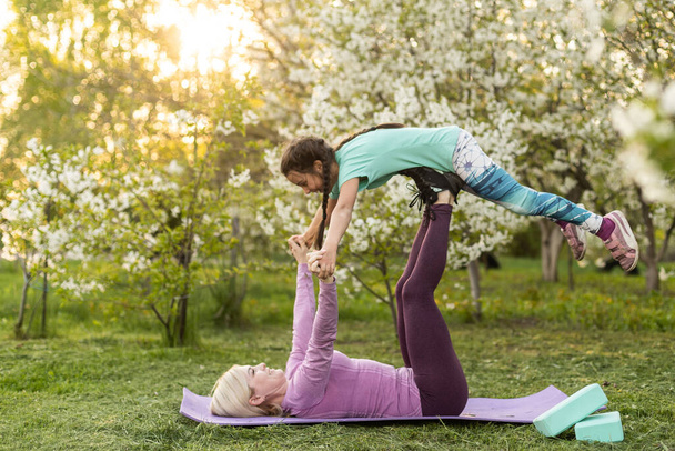 a young mother and daughter perform yoga exercises in the park on a gym mat. healthy lifestyle - Foto, imagen