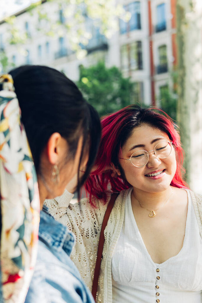 Close-up of a young Japanese girl with red hair talking to her friend naturally. Woman 20s relaxing outdoors smiling with her friend. - Photo, image