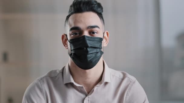 Estudante masculino étnico empresário hispânico cara em máscara médica proteger contra surto de coronavírus posando dentro de casa mostrando polegares para cima como gesto recomenda vacinação saudável imunização prevenir vírus - Filmagem, Vídeo