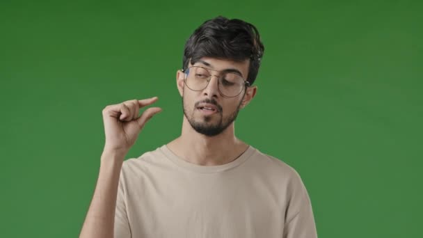 Απογοητευμένη δυστυχισμένη μελαχρινή αραβική άνθρωπος κάνει λίγο χειρονομία με τα δάχτυλα δυσαρεστημένος τύπος δείχνουν μικρό μέγεθος σχήμα χαμηλή βαθμολογία μέτρησης ιντσών μικροσκοπική κλίμακα στέκεται απομονωμένο εσωτερικό σε πράσινο φόντο - Πλάνα, βίντεο