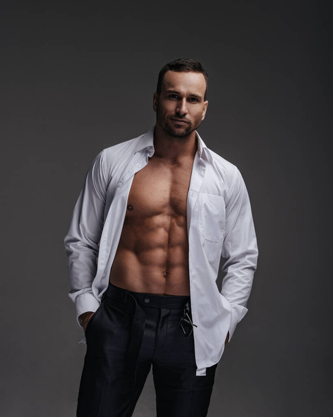 Handsome and successful sexy man stands in studio with his shirt unbuttoned - Photo, Image
