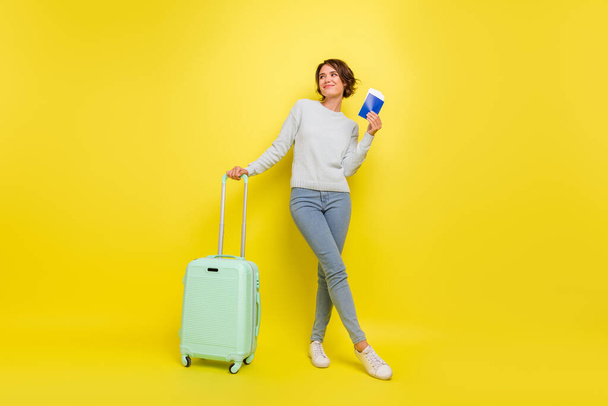 Photo of dreamy lady hold passport case look empty space wear blue sweater jeans shoes isolated yellow color background. - Фото, зображення