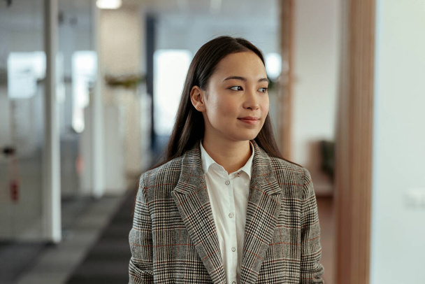 Çekici Asyalı iş kadınının modern ofiste dikilip bakışlarını kaçırması. - Fotoğraf, Görsel