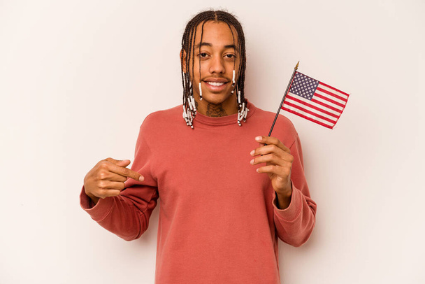 Молодой афроамериканец с американским флагом на белом фоне указывает рукой на пространство для копирования рубашки, гордый и уверенный в себе - Фото, изображение