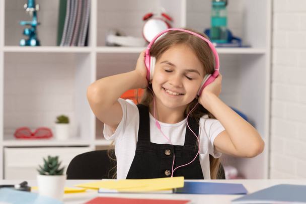 笑顔の子供は学校の教室でヘッドフォンで音楽を聞く. - 写真・画像