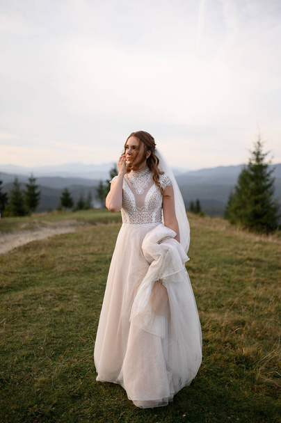 Beautiful bride in a white wedding dress on a background of mountains. - Zdjęcie, obraz